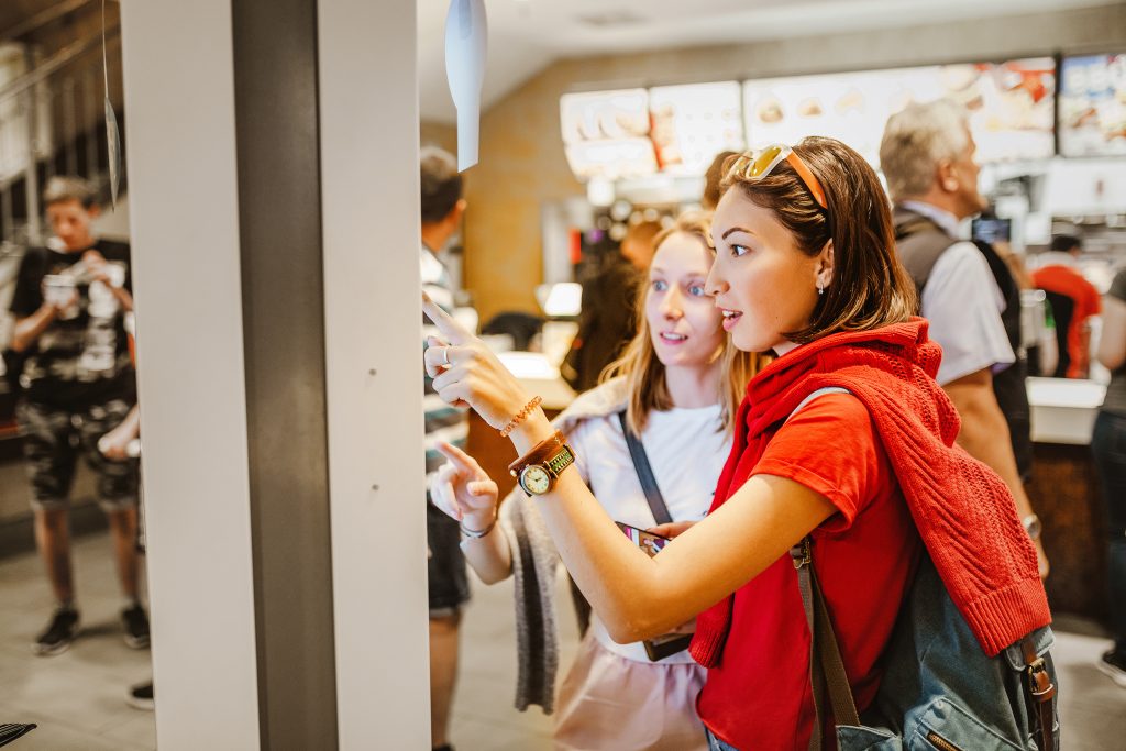 Two ladies using a touchscreen ordering kiosk in a fast-food restaurant