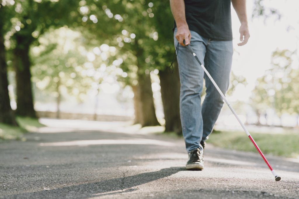 Visually impaired person walking outdoor with a white cane.