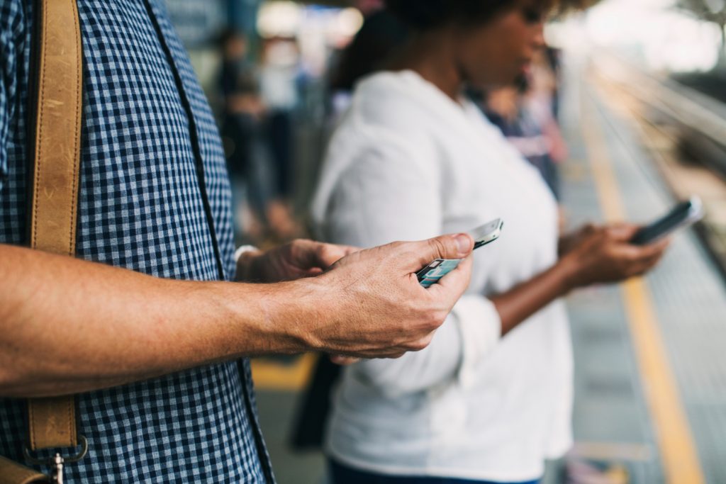 People using smartphones while waiting on a train platform.